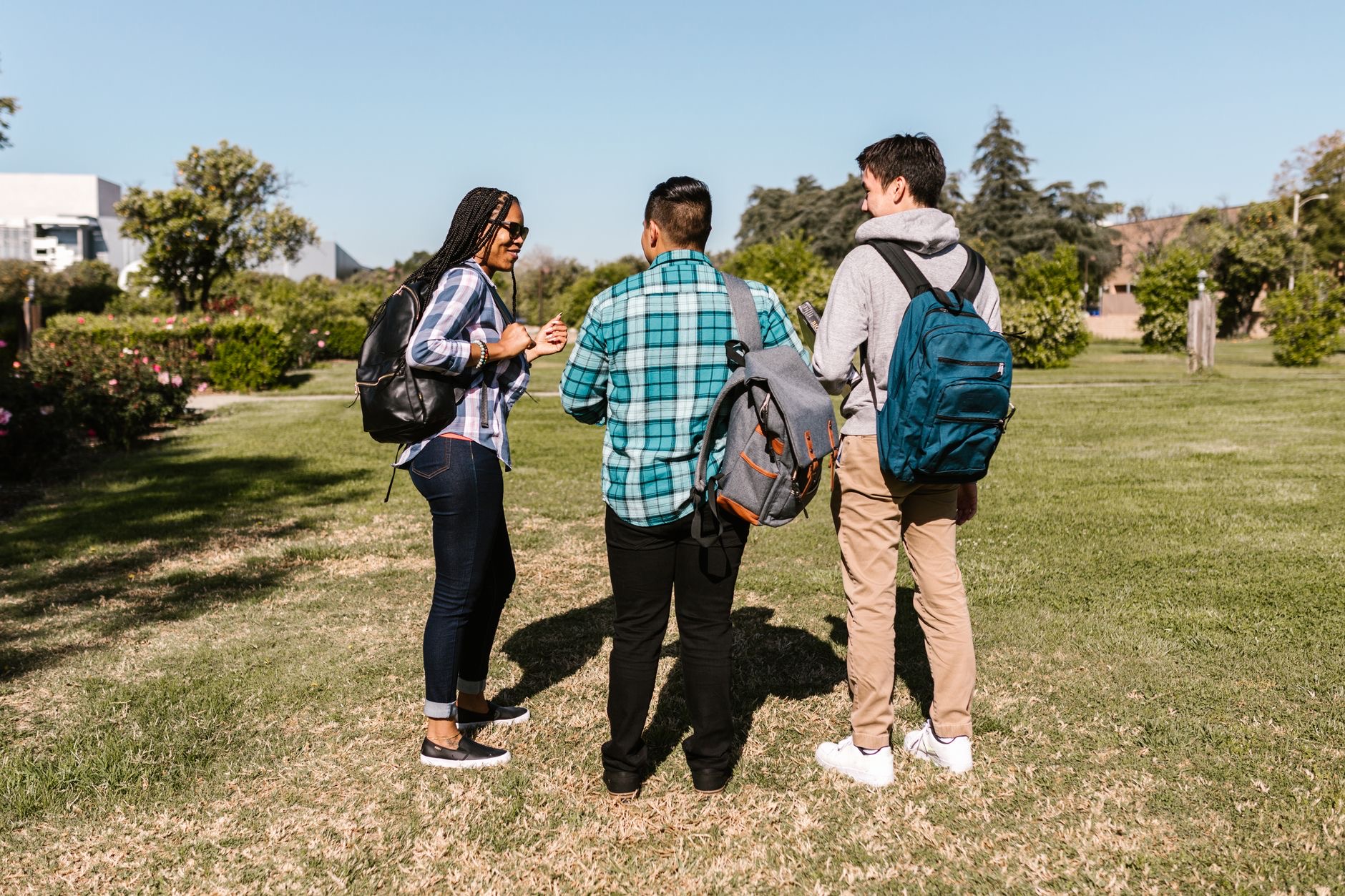 A student parent walks across a college campus with a child while carrying books and a backpack.